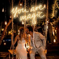 a bride and groom kissing in front of a neon sign that says you are magic