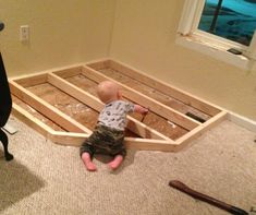 a baby is sitting on the floor in front of a wooden frame that is being built