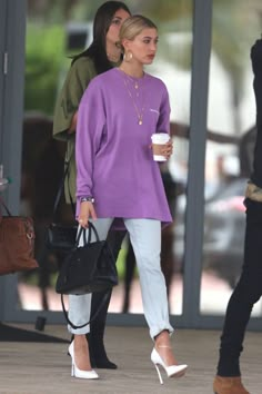 two women in purple sweaters and white pants are walking down the street with coffee