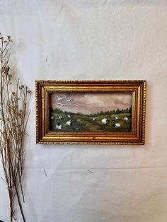 a painting hanging on the wall next to a vase with flowers in it and a plant