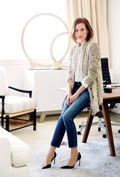 a woman sitting on top of a chair in front of a desk with a laptop computer