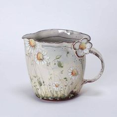 a white and brown cup with flowers painted on the side, sitting in front of a white background