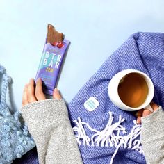 a person holding a bar next to a cup of tea and a blue blanket on a table