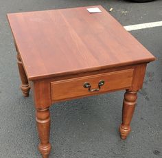 a small wooden table with two drawers on it's sides, in the middle of a parking lot