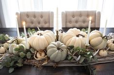 a table topped with lots of white pumpkins and greenery on top of it