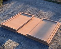 two wooden trays sitting on top of a gravel road next to grass and bushes