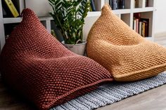 two knitted pillows sitting on top of a wooden floor next to a potted plant