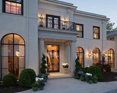 a large white house with lots of windows and plants on the front lawn at dusk