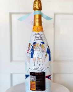 a bottle of champagne is decorated with pictures and ribbons on the top, while sitting on a table in front of a white door