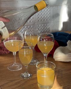 three wine glasses filled with yellow liquid are sitting on a table next to an empty bottle