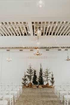 the ceremony room is decorated with white chairs and pine trees