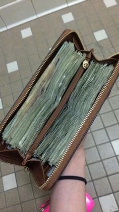 a woman's hand holding a wallet full of money in front of tiled floor