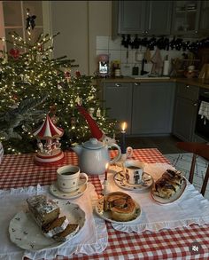 a table topped with plates and cups filled with cake next to a christmas tree covered in lights