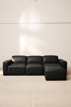 a black leather couch sitting on top of a white floor next to a wall and window