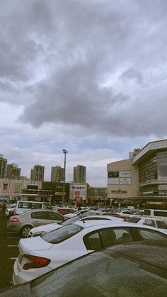 cars are parked in a parking lot with buildings in the background and cloudy skies overhead