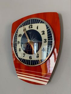 a red clock mounted to the side of a wall next to a white and black striped wall