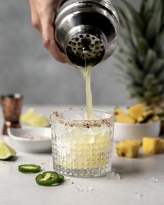 a person pours a drink into a glass filled with ice and lime slices on the side