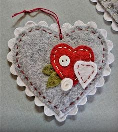 two felt heart ornaments with buttons and laces on the edges, one is red and the other is grey