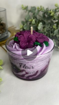 a glass bowl filled with purple flowers on top of a white table next to plants