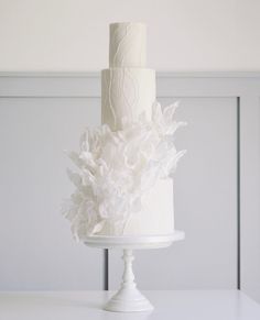 a white wedding cake with flowers on the top and bottom is sitting on a pedestal