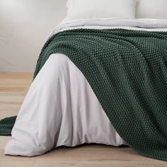 a bed with a green blanket and white pillows on top of it, next to a wooden floor