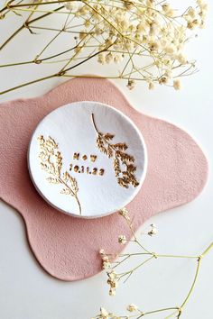 a white plate with gold lettering on it sitting next to some dried flowers and pink placemats