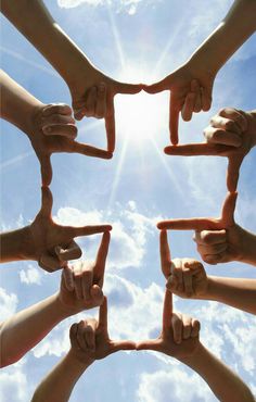 several hands making a star shape with their fingers in the air against a blue sky