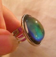 a person is holding a ring with an oval shaped rainbow stone in it's center