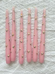 five pink candles with daisies on them sitting on a white doily covered table