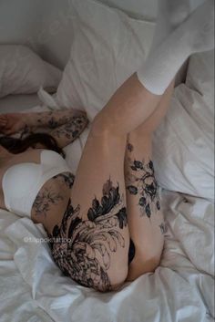 a woman laying on top of a bed covered in white sheets and tattoos next to her legs