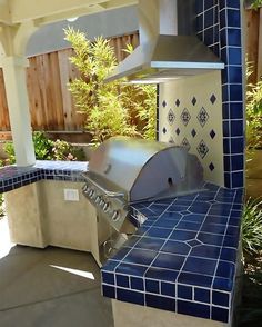 an outdoor kitchen with blue tiles on the counter and hood over it's grill