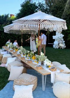 an outdoor table set up for a party with white pillows and flowers on the ground