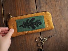 a hand holding a pair of scissors next to a small pouch with a leaf on it