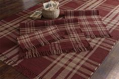 a red and white plaid rug with fringes on the floor next to a basket