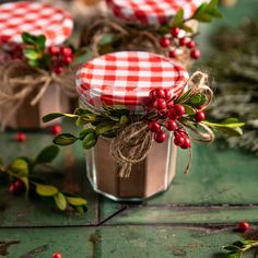 three small jars with red and white checked lids are sitting on a green tablecloth