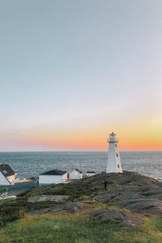 a lighthouse on top of a hill next to the ocean at sunset or sunrise with people walking around it