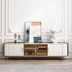 a white and gold entertainment center with art on the sideboard in an empty room