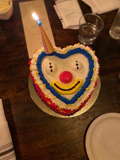 a birthday cake with a clown face on it and a lit candle in the shape of a heart