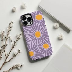 an iphone case with purple and yellow daisies on it, next to some flowers