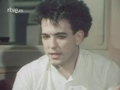 a man in white shirt sitting down with his hand on his hip and looking at the camera