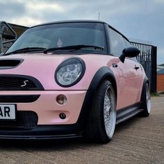 a pink mini car parked in front of a fenced area with a black gate