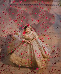 a woman in a white and gold wedding dress surrounded by rose petals on the floor