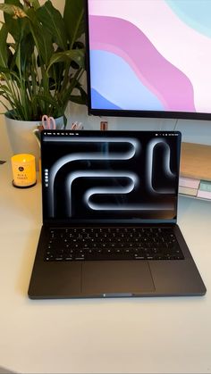 an open laptop computer sitting on top of a white desk next to a potted plant