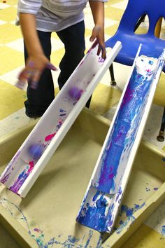 a child is painting on an easel with blue and pink paint, while another child stands in the background