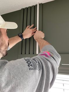 a man wearing a white hat and gray shirt is fixing the shutters on a window