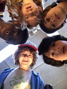 four children are standing in a circle looking up at the camera with their heads together