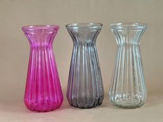 three different colored glass vases sitting next to each other on a tableclothed surface