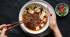 two hands holding chopsticks over a bowl of food on a black tablecloth