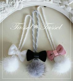 three bows and two pom poms hanging from a white frame with the words tasseled on it