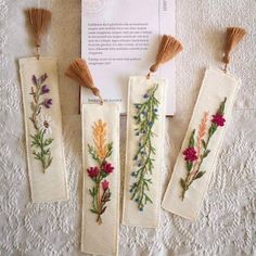 three embroidered bookmarks with tassels and flowers on them sitting on a table